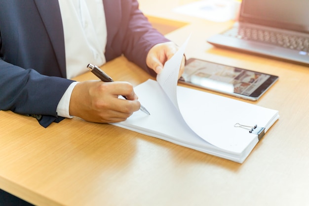 Businessman signing contract paper with pen in office desk.