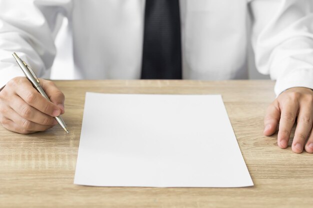 Фото Бизнесмен сидит за столом с ручкой в руке и пустым листом белой бумаги