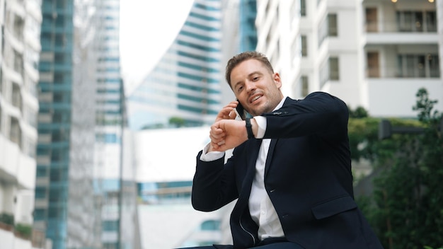 Businessman sitting at bench while talking to manager by using phone Urbane