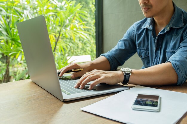 Businessman sitting at cafe working on klaptop with smartphone and paperwork on table