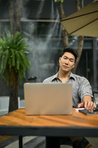 A businessman sitting at a coffee shop in an outdoor space with his laptop