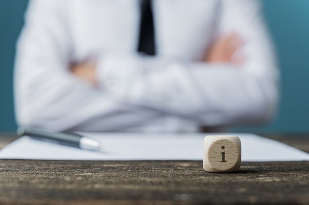 Businessman sitting at his desk with pen and paper in front of him and a dice wit letter i on it