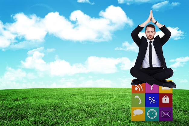 Businessman sitting in lotus pose with hands together against blue sky over green field