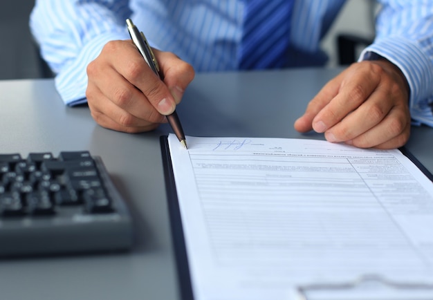 Businessman sitting at office desk signing a contract with shallow focus on signature.