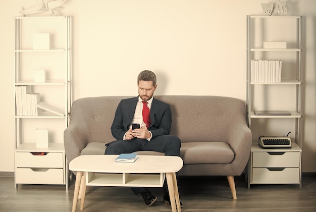 Businessman sitting in office and texting on phone