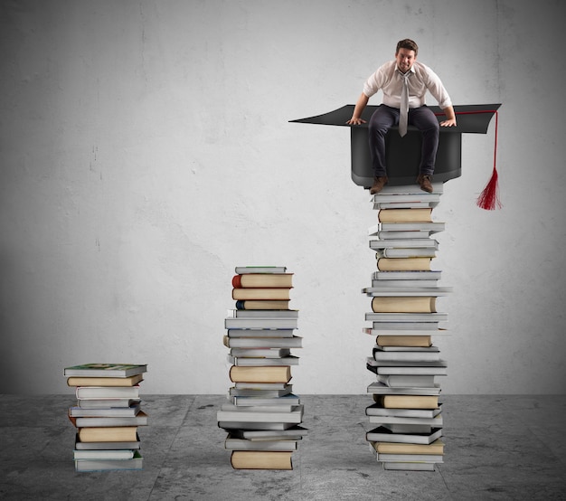 businessman sitting on a pile of books with graduation cap