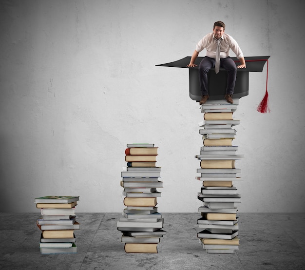 Foto uomo d'affari seduto su una pila di libri con tappo di laurea