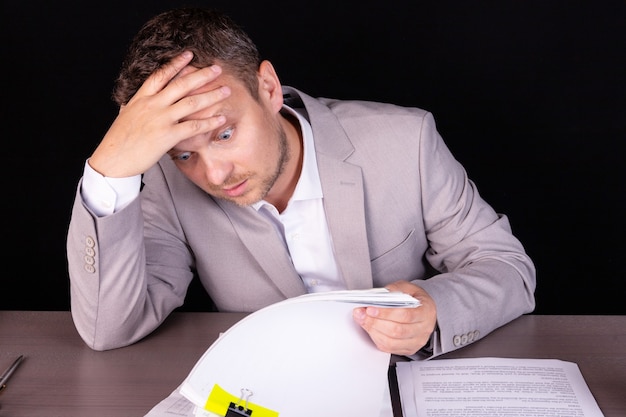 Businessman sitting at the table. On the table stacks of folders with documents.