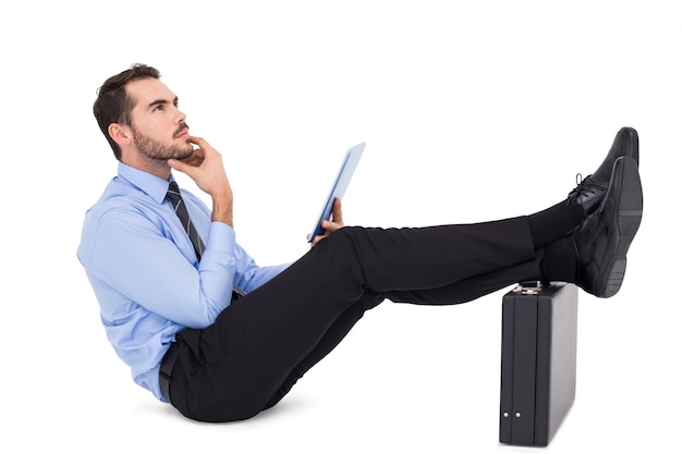 Businessman sitting with feet on his briefcase thinking 