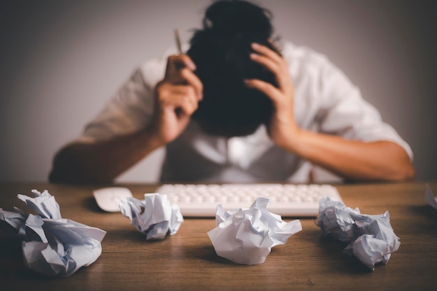 Businessman sitting with head in hands at desk covered crumpled papers. Office worker tired of too much difficult unproductive work. Stressed male entrepreneur has no idea what to do with problem