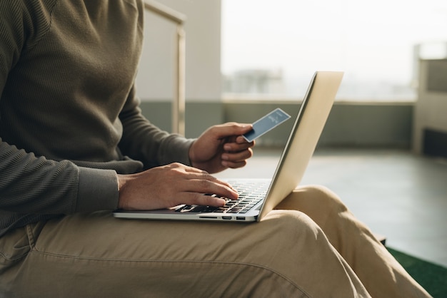 A businessman sitting with the laptop on his knees and hand takes the card