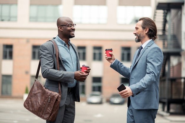 ビジネスマンの笑顔。同僚と話し、コーヒーを飲みながら笑顔のひげを生やした実業家