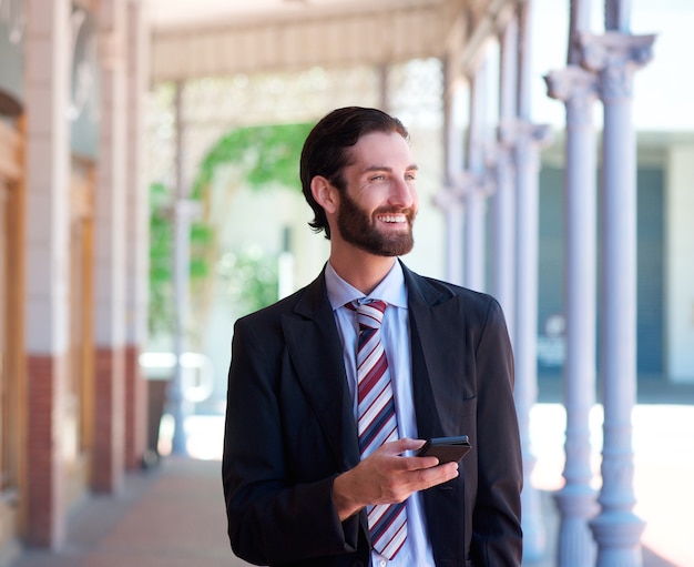 Uomo d'affari che sorride all'aperto con il telefono cellulare