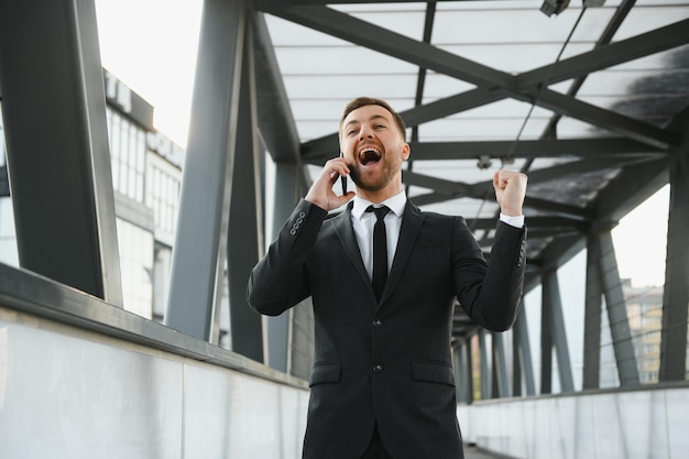 Businessman smiling and raising his fist in the air with office building background business success achievement and win concepts