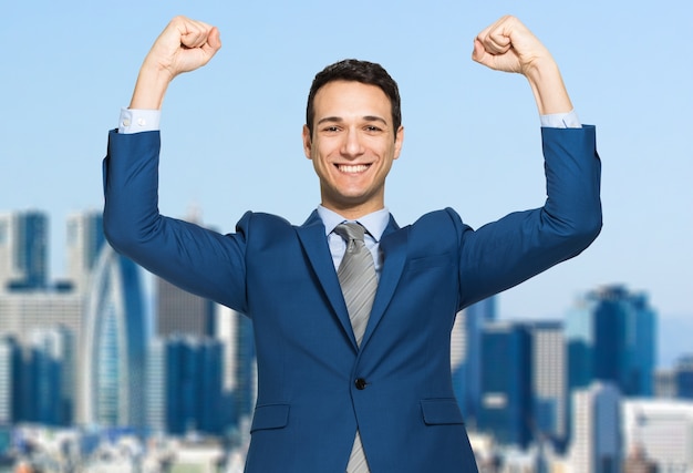 Businessman smiling and raising his fist in the air, with office building in background 