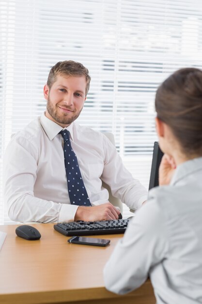 Businessman smiling with a co worker sitting at his desk