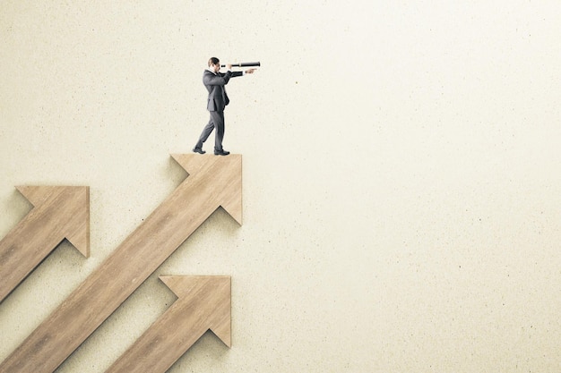 businessman standing on abstract wooden arrow and using telescope