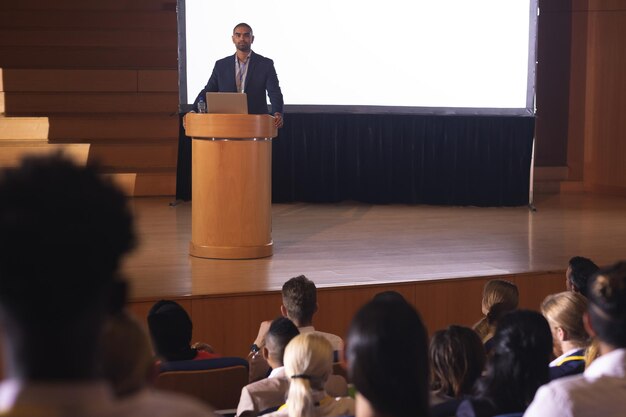 Photo businessman standing around the podium and giving speech in front of audience in the auditorium