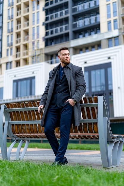 Бизнесмен, стоящий рядом со скамейкой в формальной одежде Мужчина в костюме, стоящий рядом со скамейкой