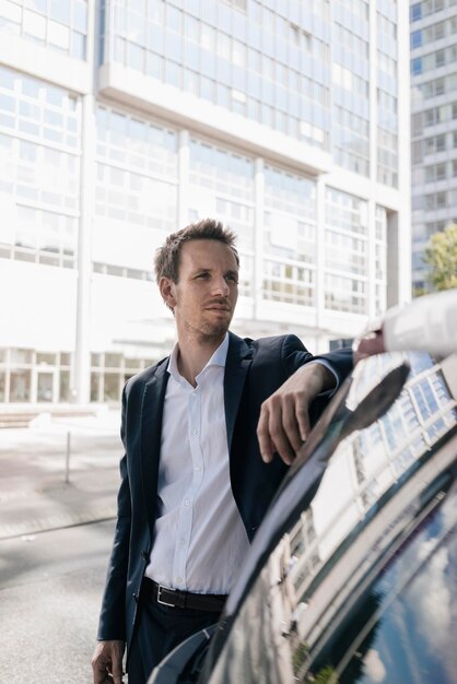 Бизнесмен, стоящий рядом с автомобилем с отражением офисной башни