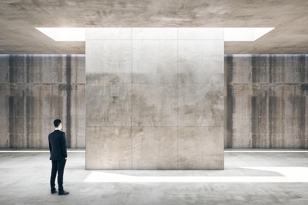 Businessman standing in concrete gallery interior with empty wall