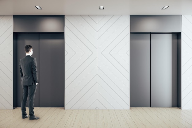 Businessman standing in contemporary office hall with two elevators