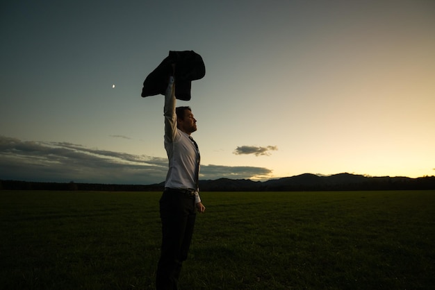 Businessman Standing in the Field and Raising his Arm with Coat