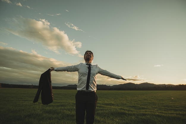 Businessman standing in green meadow with his arms spread widely