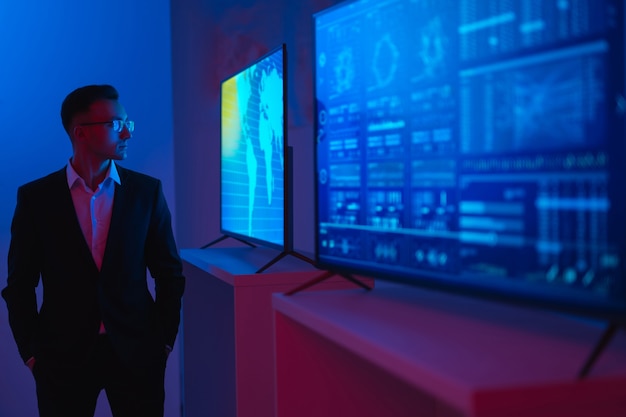 The businessman standing near screens with graphs