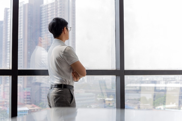 Businessman standing in office with hands crossed looking through window building