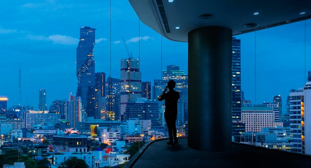 Businessman standing using smart phone in modern space watching city night view