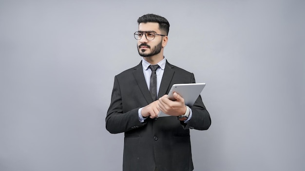 businessman standing wearing glasses holding tab looking left in black suit indian pakistani model