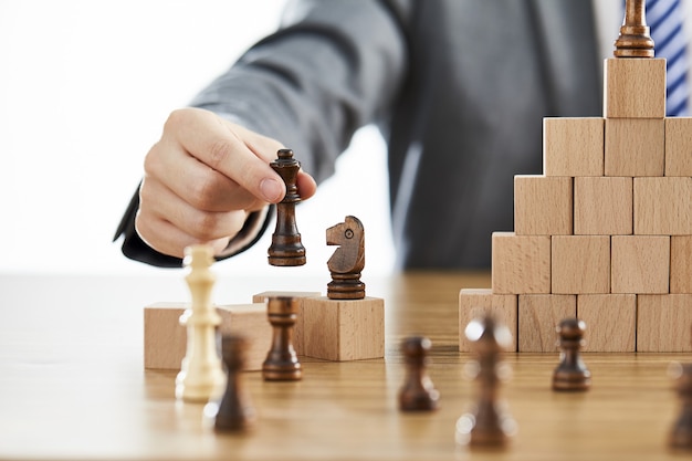 Photo businessman in a suit arranging chess pieces on wooden blocks on different levels