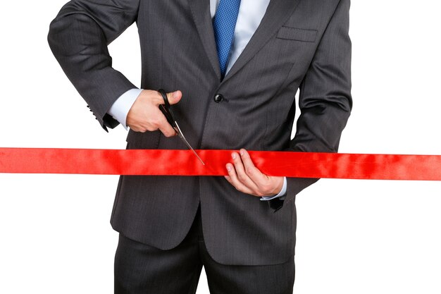 Businessman in suit cutting red ribbon with pair of scissors