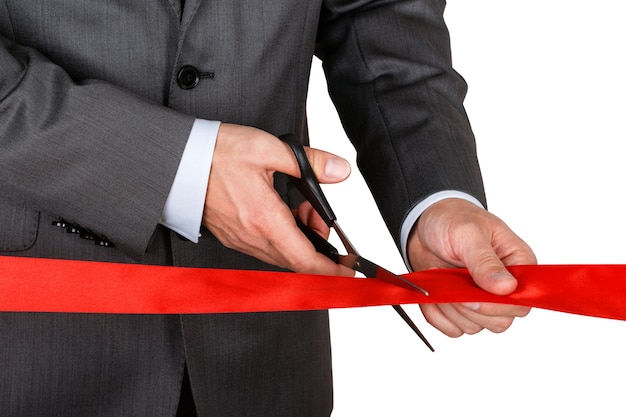 Businessman in suit cutting red ribbon with pair of scissors