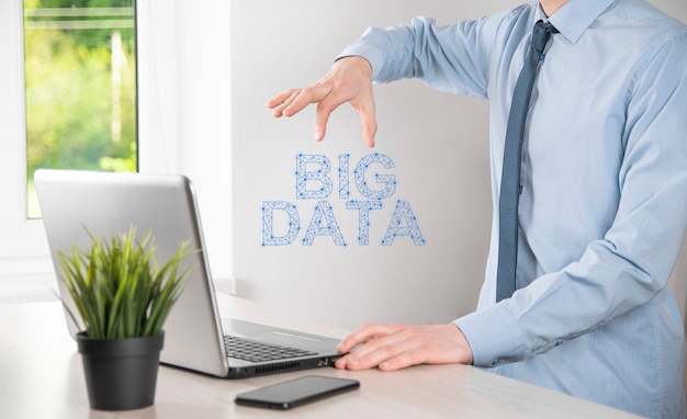 Businessman in a suit on a dark background holds the\
inscription big data. storage network online server concept.social\
network or business analytics representation