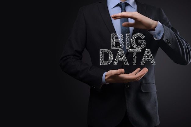 Businessman in a suit on a dark background holds the inscription BIG DATA. Storage Network Online Server Concept.Social network or business analytics representation