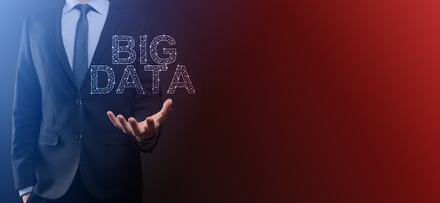 Businessman in a suit on a dark background holds the inscription BIG DATA. Storage Network Online Server Concept.Social network or business analytics representation.