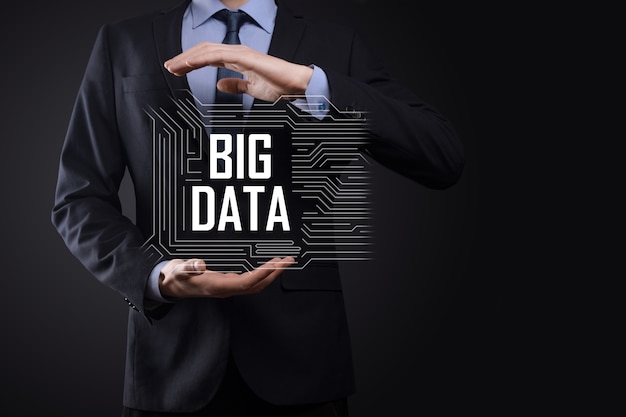 Businessman in a suit on a dark background holds the inscription BIG DATA. Storage Network Online Server Concept.Social network or business analytics representation.