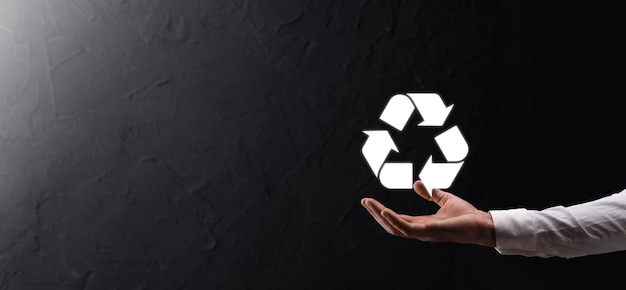 Businessman in suit over dark background holds an recycling
icon, sign in his hands. ecology, environment and conservation
concept. neon red blue light