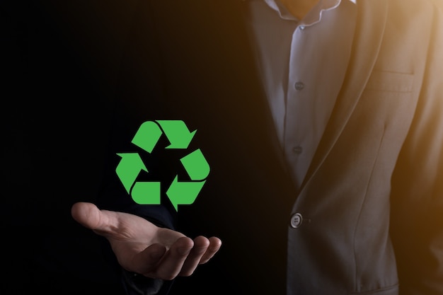 暗い背景にスーツを着たビジネスマンは、リサイクルアイコンを保持し、彼の手にサインします。エコロジー、環境、保全の概念。ネオンレッドブルーライト