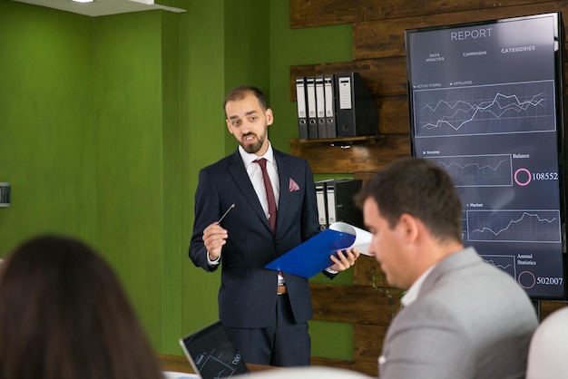 Businessman in suit explaning his plan with charts on tv screen in the conference room. Corporate meeting.