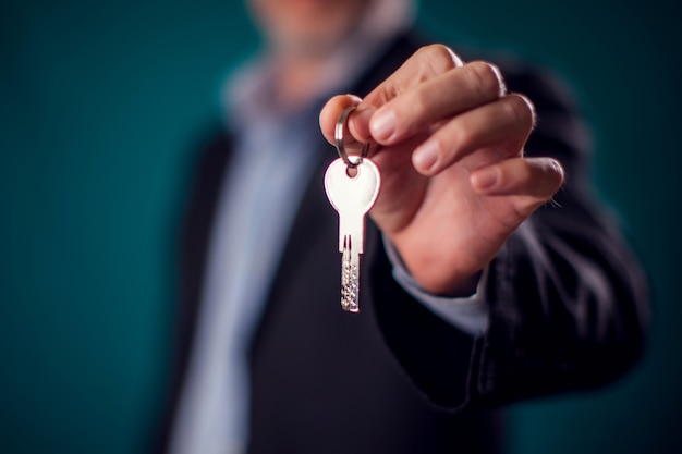 Businessman in suit holding house key in hand. Mortgage, credit or property concept