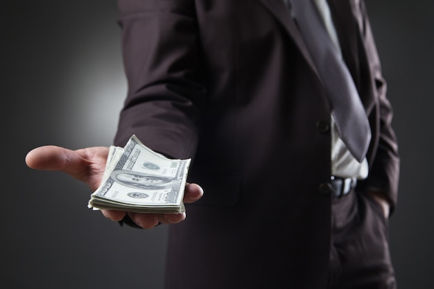 Businessman in suit holding money on dark