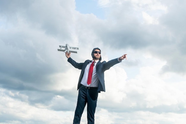 Бизнесмен в костюме и шляпе пилота запускает игрушку на фоне неба