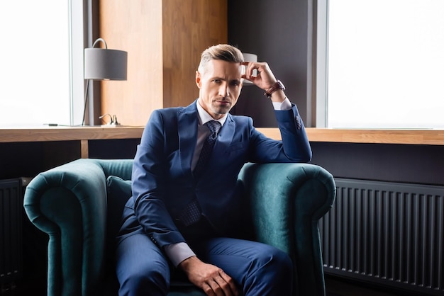 Businessman in suit sitting in armchair and looking at camera