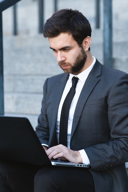 Businessman in a suit sitting on the steps and working on a laptop.