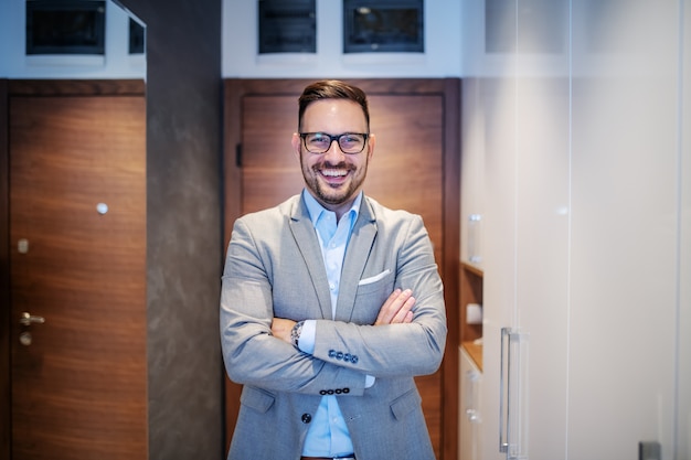 Businessman in suit standing at home in hall with folded arms.