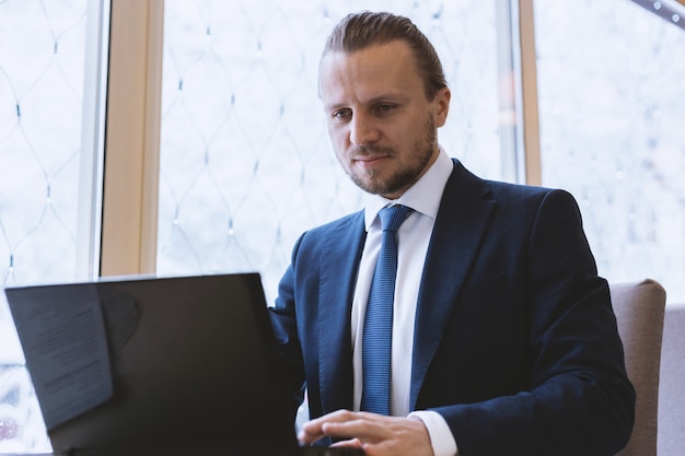 Businessman in the suit  working on the laptop sitting  at the table indoor