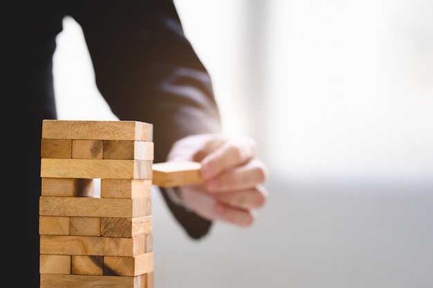 Businessman take and picking wood block on stacked tower by hand as startup project